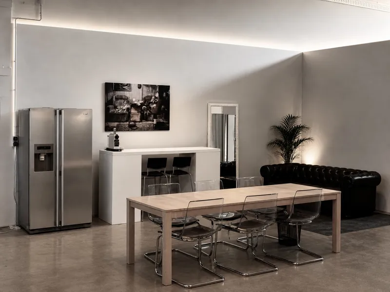 Lounge Bereich mit Esstisch, Stühlen, Küchenzeile, Kühlschrank, Kaffeemaschine und schwarzem Sofa, Palme, entspannen, relax.